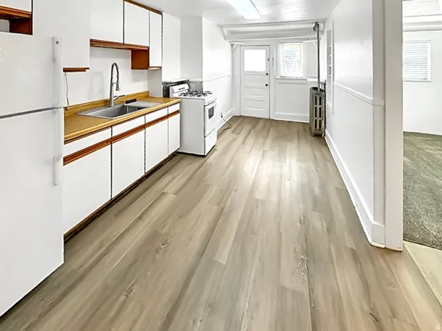 Kitchen featuring dual tone cabinets, white appliances, light wood finished floors, light countertops, and radiator