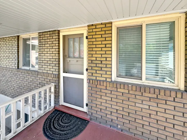 Doorway to property with brick siding and a porch
