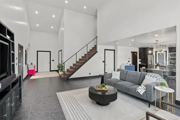 Modern open-concept living space featuring soaring ceilings with recessed lighting, a floating wood-finish staircase with metal railings, and seamless sightlines throughout