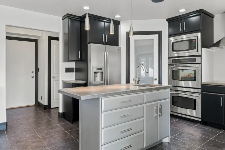 Kitchen featuring a central island with an integrated sink, dark cabinetry, stainless steel appliances, tile flooring, and recessed lighting