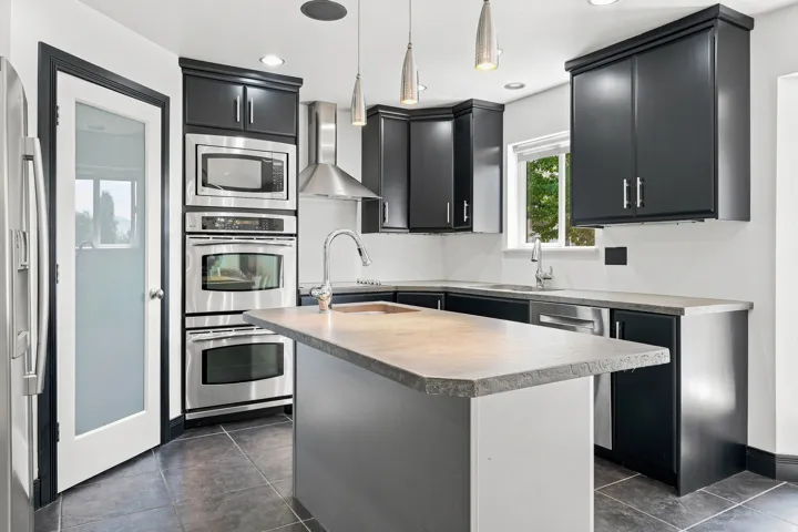 Modern kitchen featuring custom black cabinetry with stainless steel hardware, quartz countertops with waterfall edge detailing, and a generous island with seating