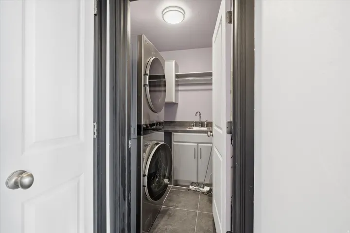 Laundry room featuring stacked washer and dryer, dark tile patterned flooring, and cabinet space