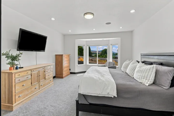 Bay window offering natural light, recessed lighting, ceiling-mounted light fixture, wall-mounted television, and light gray carpeting