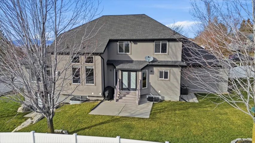 Rear view of property featuring roof with shingles, a lawn, and a patio