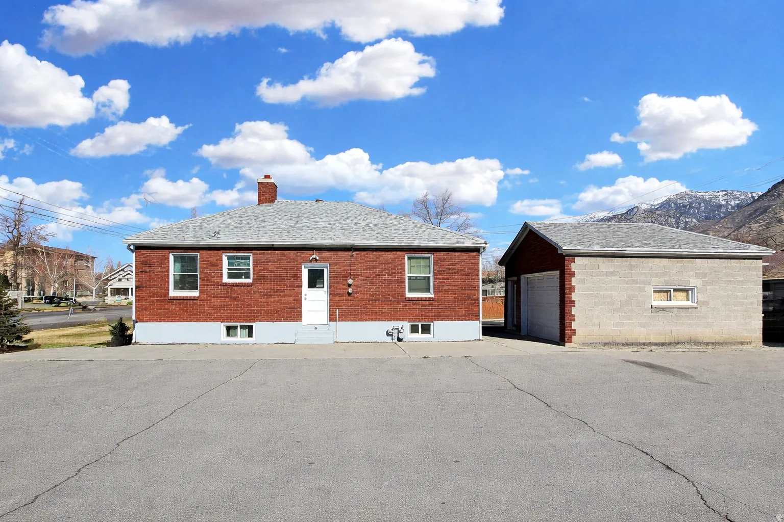 View of property exterior featuring an outdoor structure, brick siding, a chimney, a garage, and a mountain view