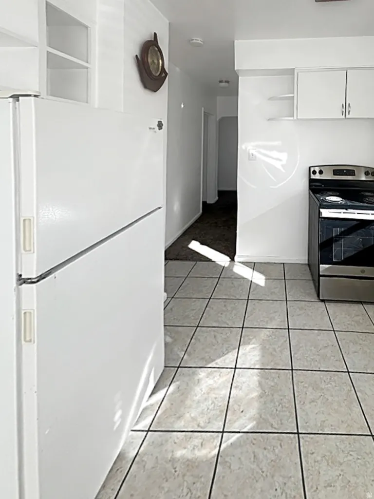 Kitchen with freestanding refrigerator, stainless steel range with electric cooktop, open shelves, white cabinetry, and light tile patterned flooring