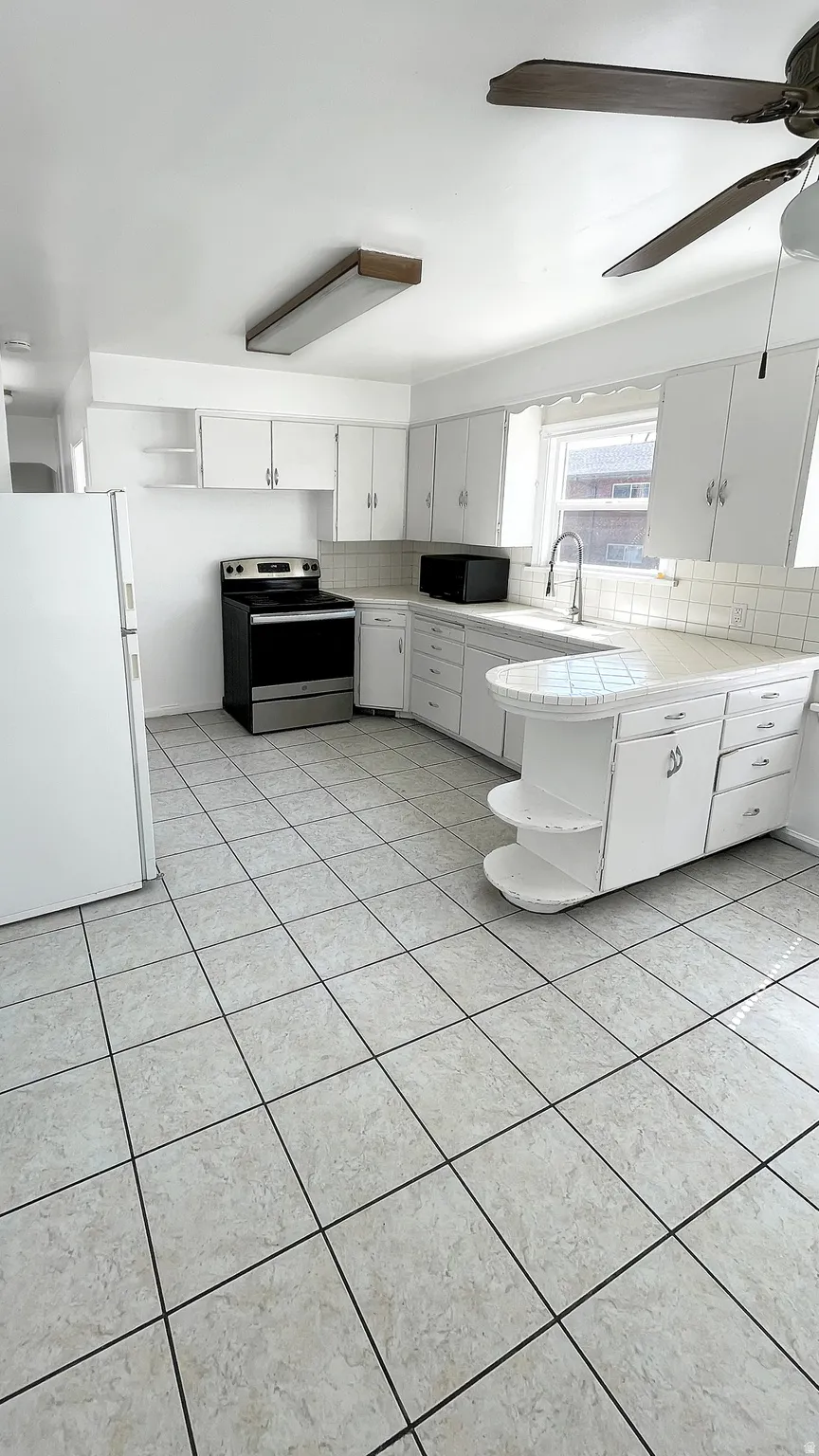 Kitchen with decorative backsplash, freestanding refrigerator, stainless steel electric range oven, and white cabinetry