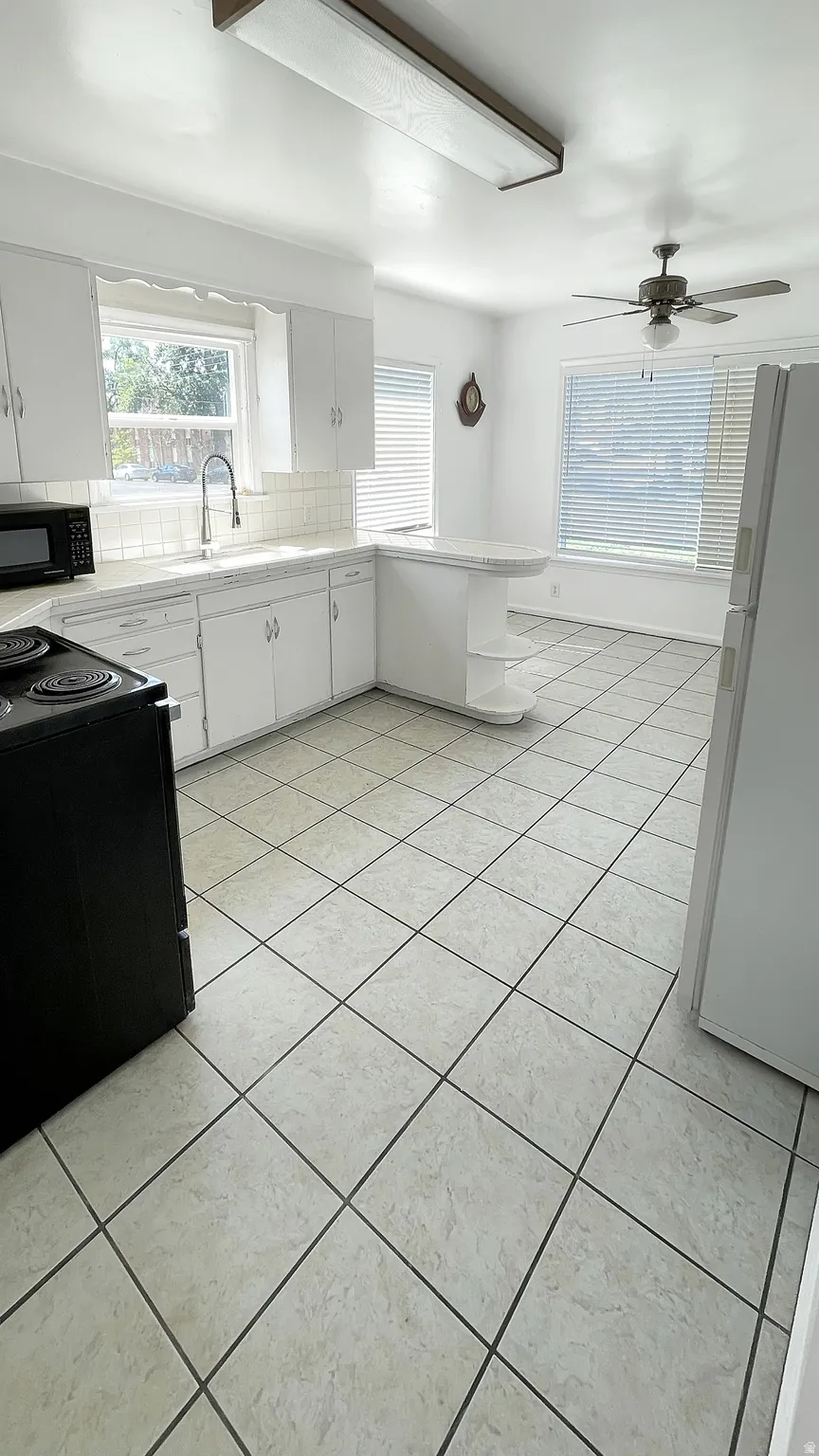 Kitchen featuring white cabinetry, black appliances, decorative backsplash, light tile patterned floors, and a peninsula