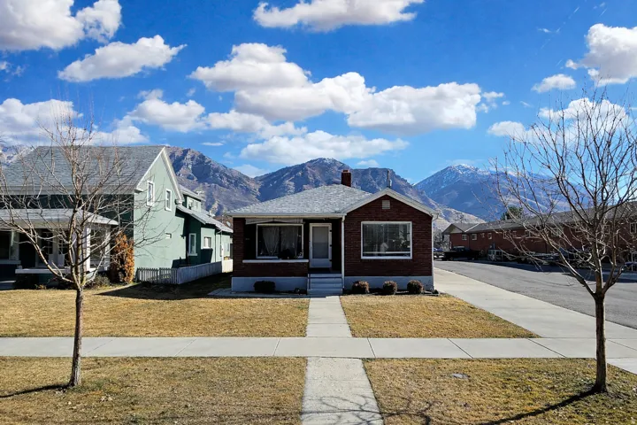 View of front of property featuring brick siding, a mountain view, a chimney, and a front yard