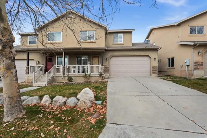 Traditional-style home with stucco siding, covered porch, concrete driveway, an attached garage, and a front yard