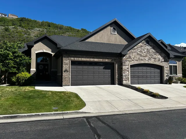 Stucco and stone exterior featuring multiple gables and a dark composition shingle roof