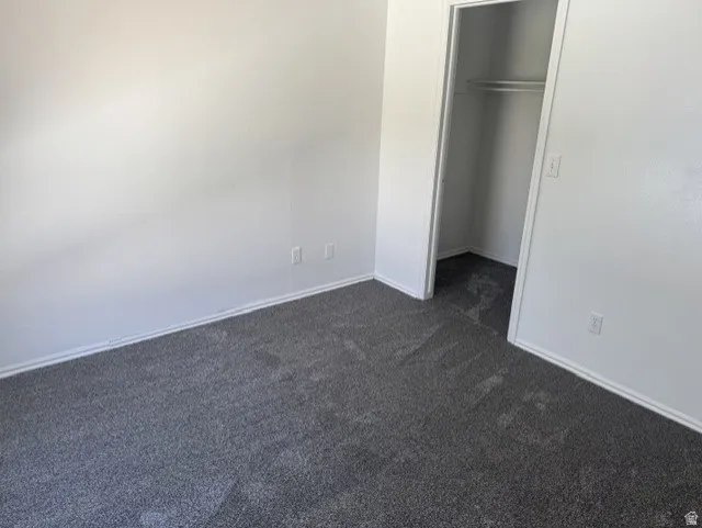 Room with light gray walls and dark gray carpet, featuring white baseboards, electrical outlets, and a closet with a built-in hanging rod
