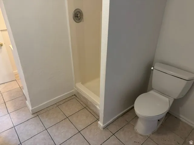 Bathroom featuring a standalone shower with a chrome fixture, a white toilet, and light-toned square tile flooring