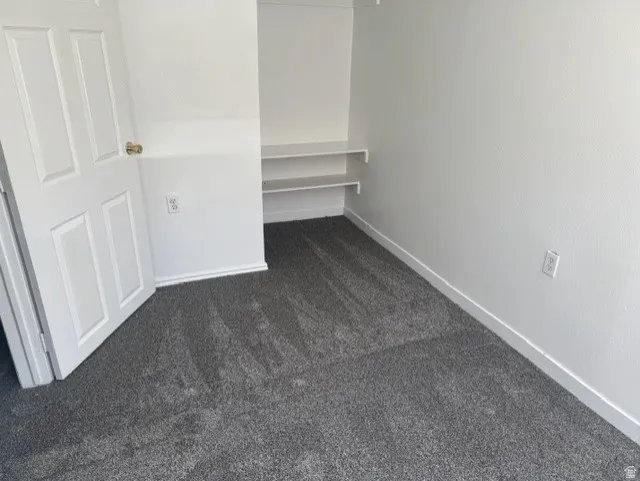 Compact room featuring built-in shelving, gray carpet flooring, white baseboards, and a white four-panel door with a brass-finish doorknob