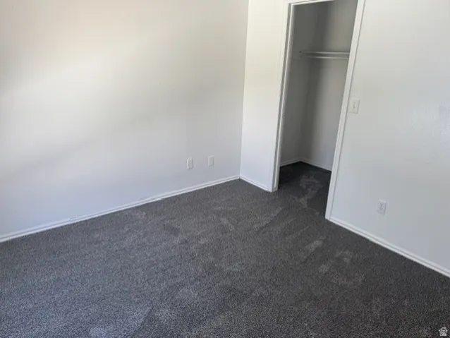 Room with light gray walls and dark gray carpet, featuring white baseboards, electrical outlets, and a closet with a built-in hanging rod