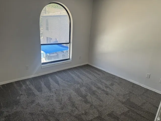 Room featuring a distinctive arched window, neutral wall paint, and gray patterned carpet flooring