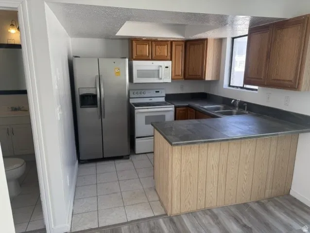 Kitchen featuring wood cabinetry, dark countertops, a stainless steel refrigerator, white range, and a dual basin sink