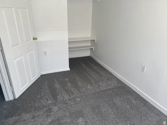 Compact room featuring built-in shelving, gray carpet flooring, white baseboards, and a white four-panel door with a brass-finish doorknob