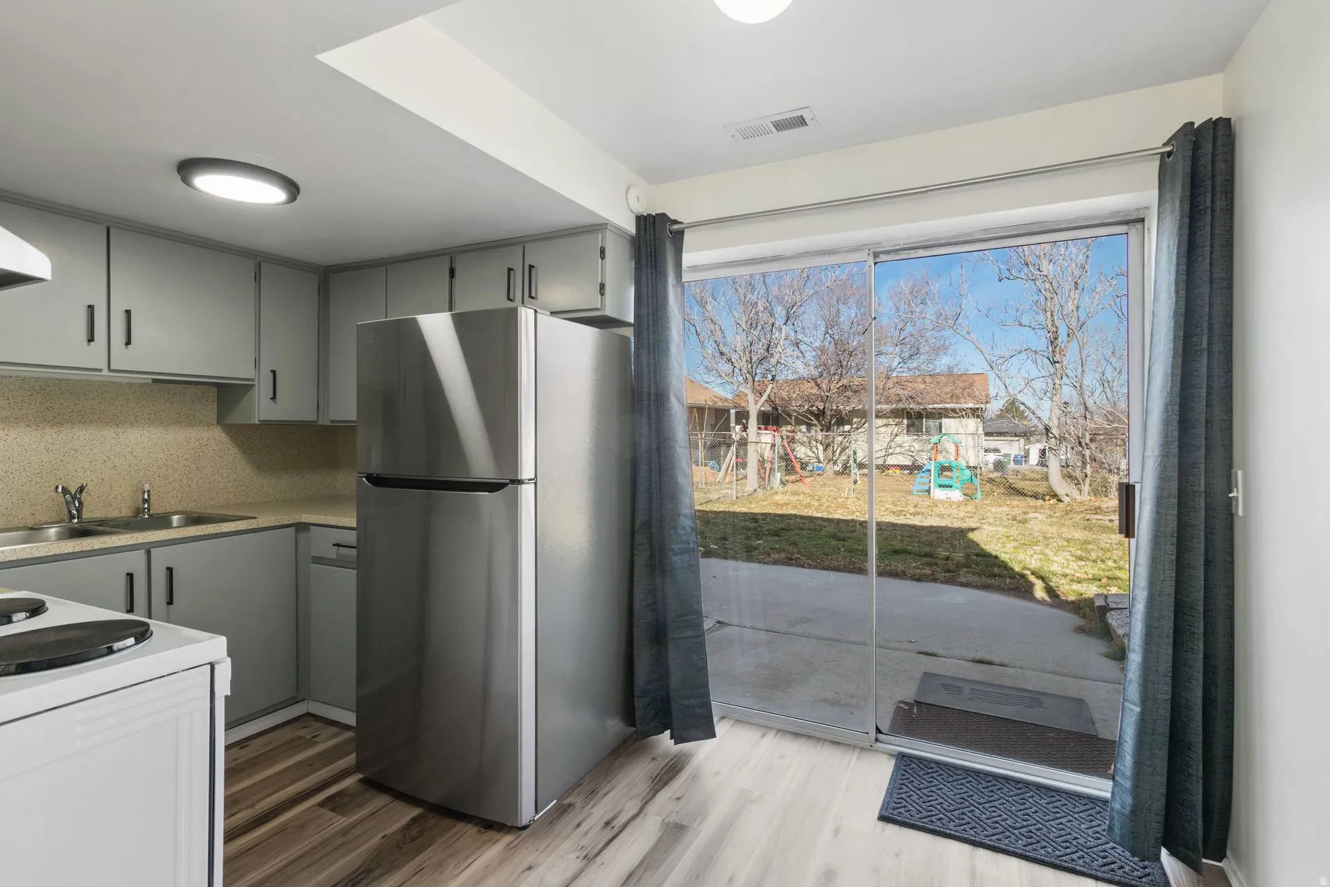Kitchen with gray cabinets, freestanding refrigerator, light countertops, light wood-style flooring, and backsplash