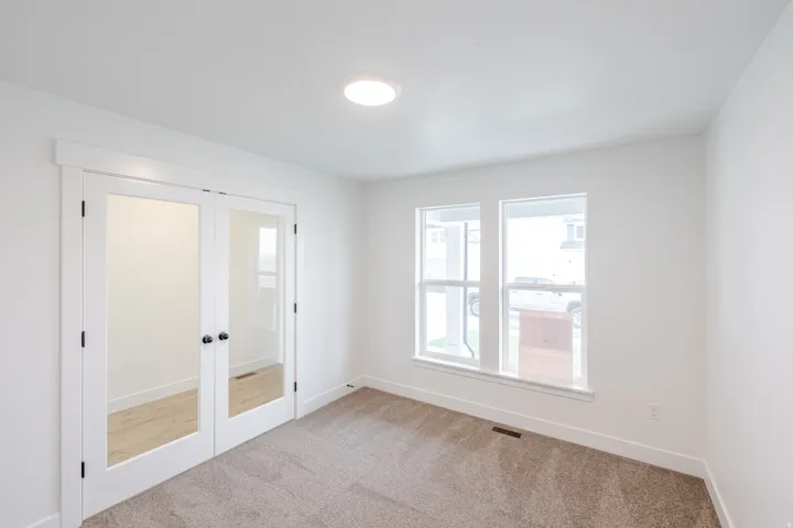 Room with French doors featuring frosted glass panels, two windows with white trim, recessed ceiling lighting, and carpet flooring