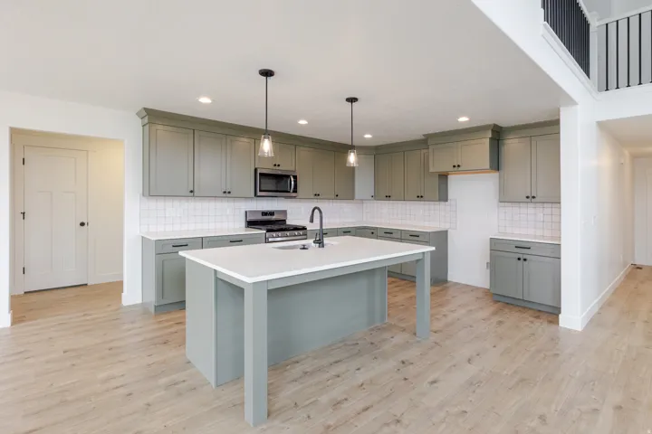 Open-concept kitchen featuring an oversized island with a white countertop, extensive sage green cabinetry, a white subway tile backsplash, stainless steel appliances, and wood-finish flooring throughout