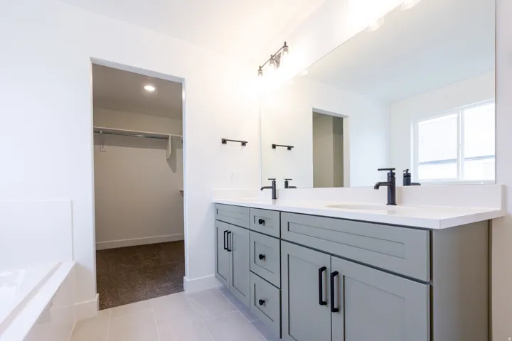 Dual vanity featuring light gray cabinetry with black hardware, white countertops, and matte black fixtures