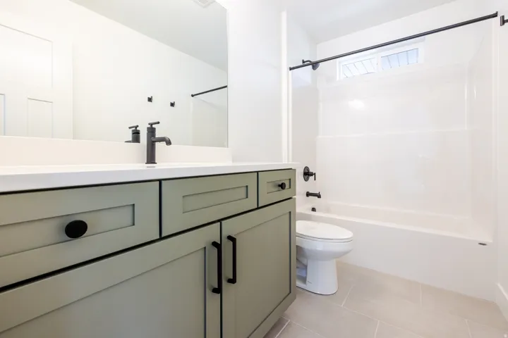 Modern bath featuring a sage green vanity with matte black hardware, white countertop, and a sleek black faucet