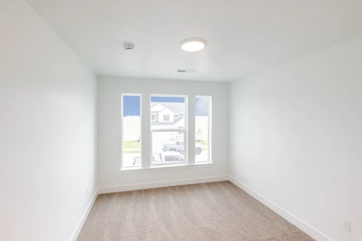 Bright interior space featuring three large windows, neutral-toned carpeting, white walls, and a ceiling-mounted light fixture