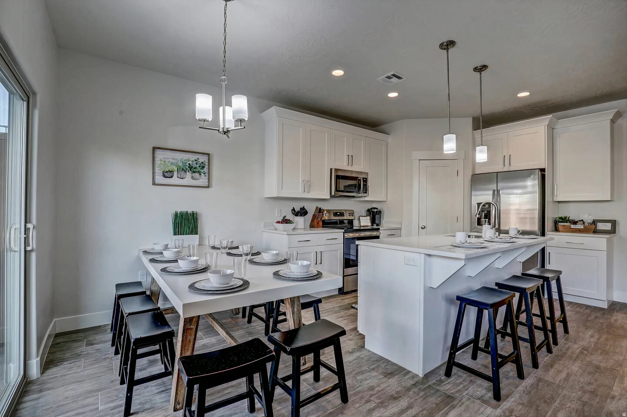 Kitchen with a breakfast bar area, stainless steel appliances, a kitchen island with sink, white cabinets, and hanging lights
