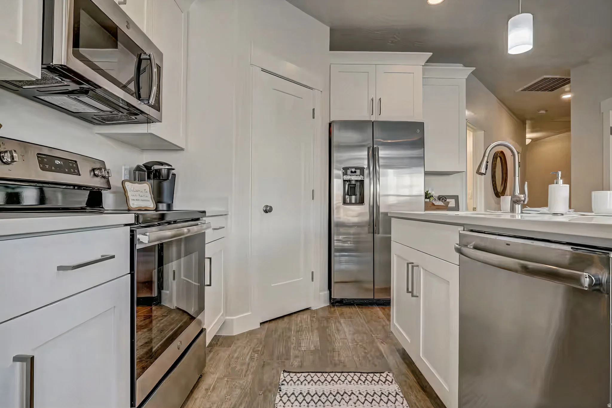 Kitchen featuring stainless steel appliances, white cabinets, hanging light fixtures, and light wood-style floors