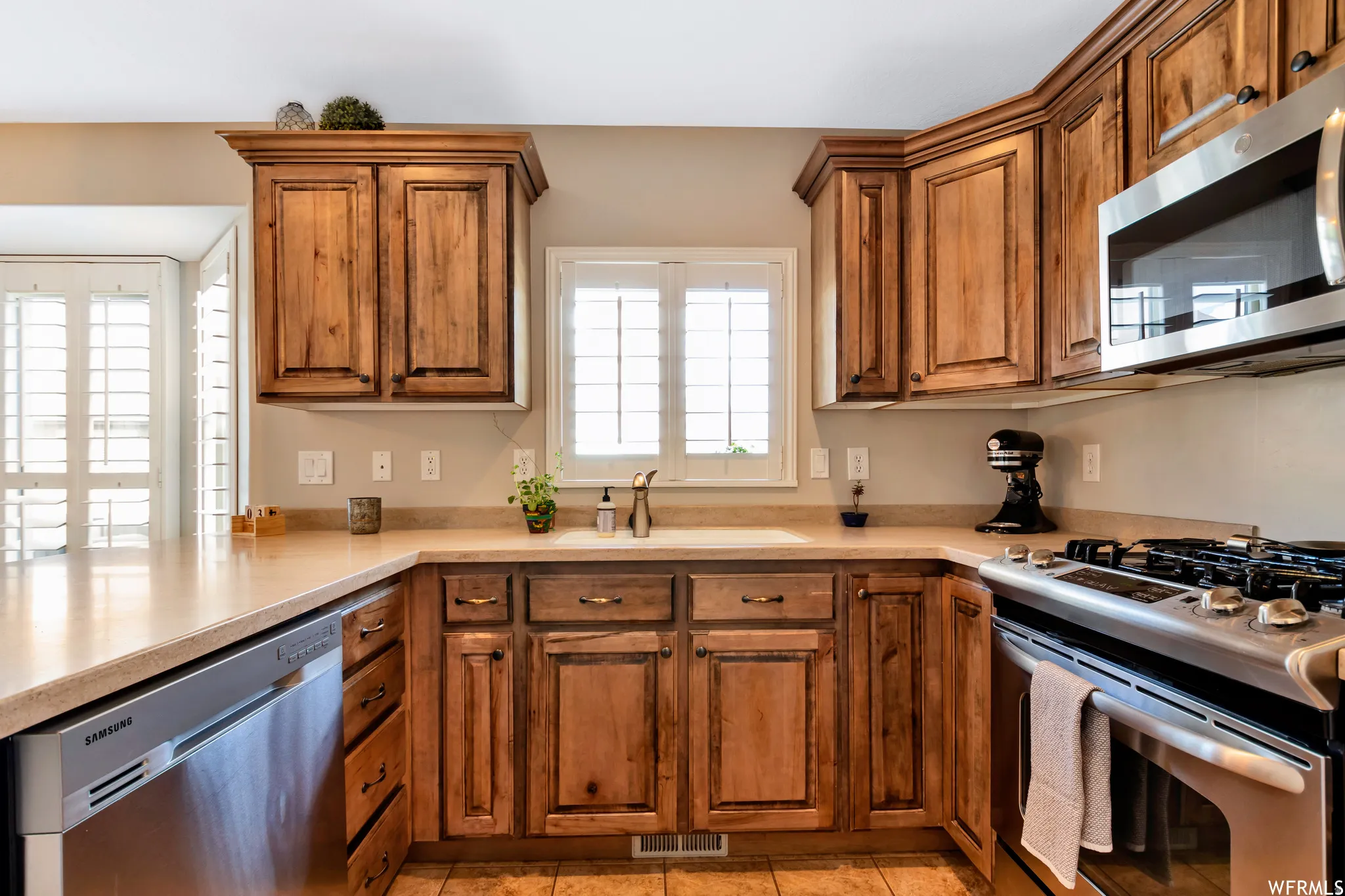 Kitchen with stainless steel appliances, wood finish cabinetry, light countertops, and a peninsula