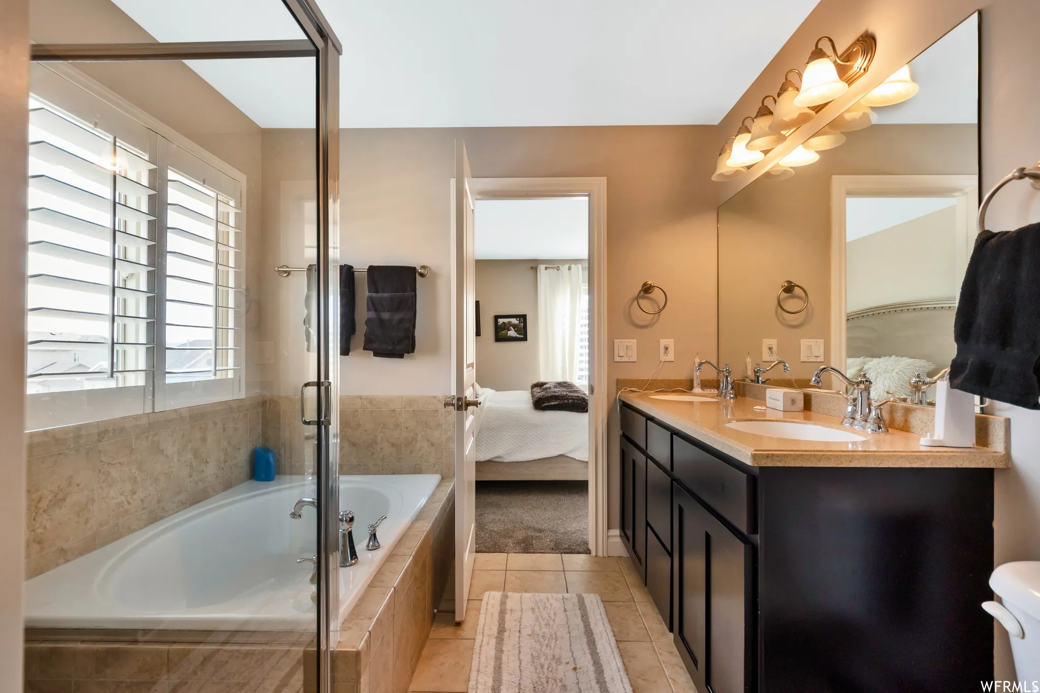 Ensuite bathroom with a garden tub, double vanity, light tile patterned floors, and a shower with door