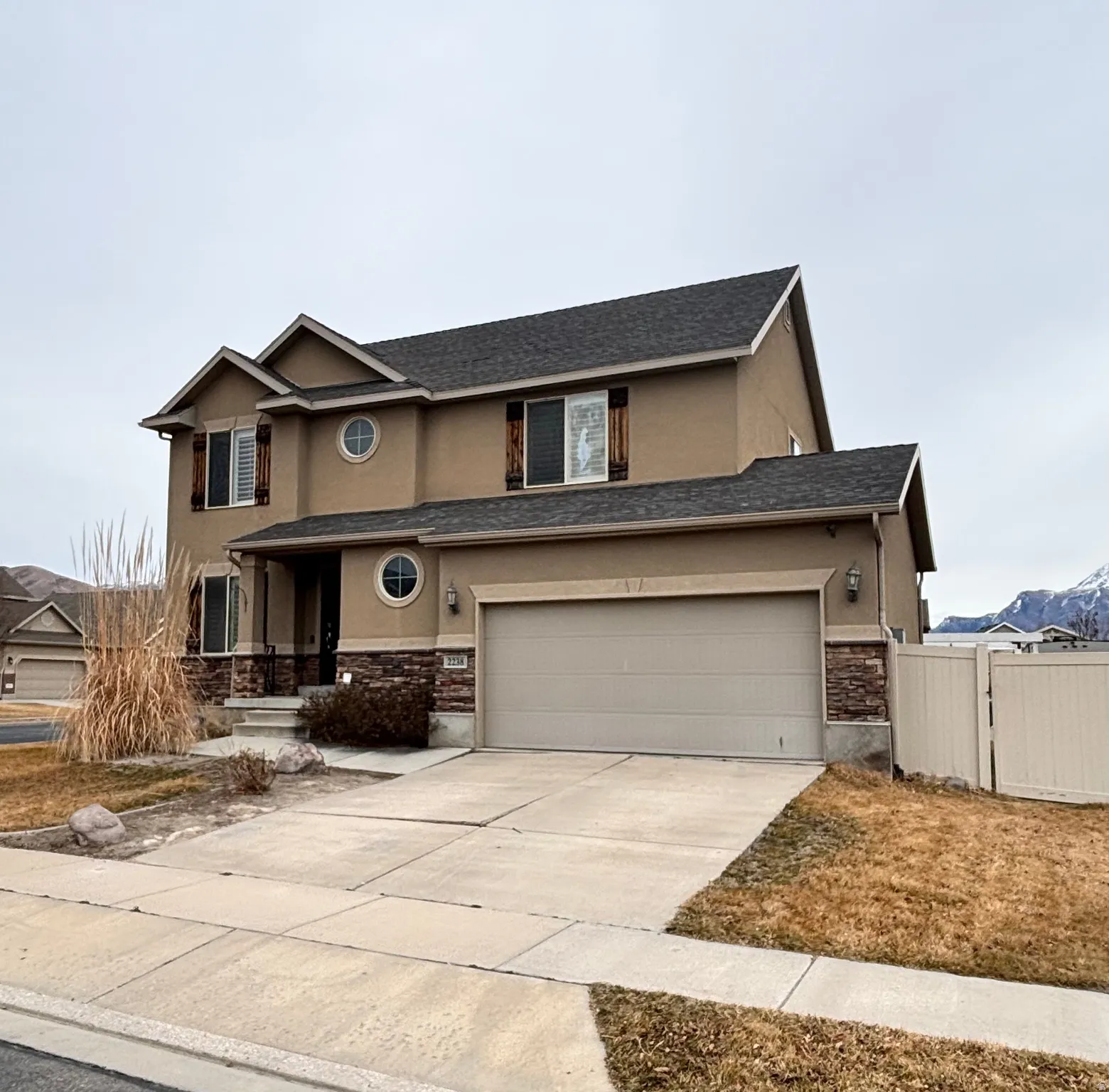 Traditional-style house featuring stucco siding, a gate, an attached garage, concrete driveway, and stone siding