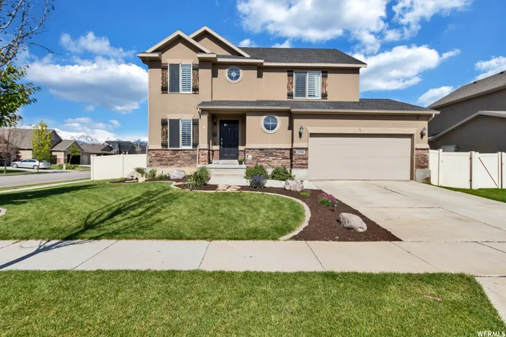 View of front facade with stucco siding, stone siding, driveway, and a gate