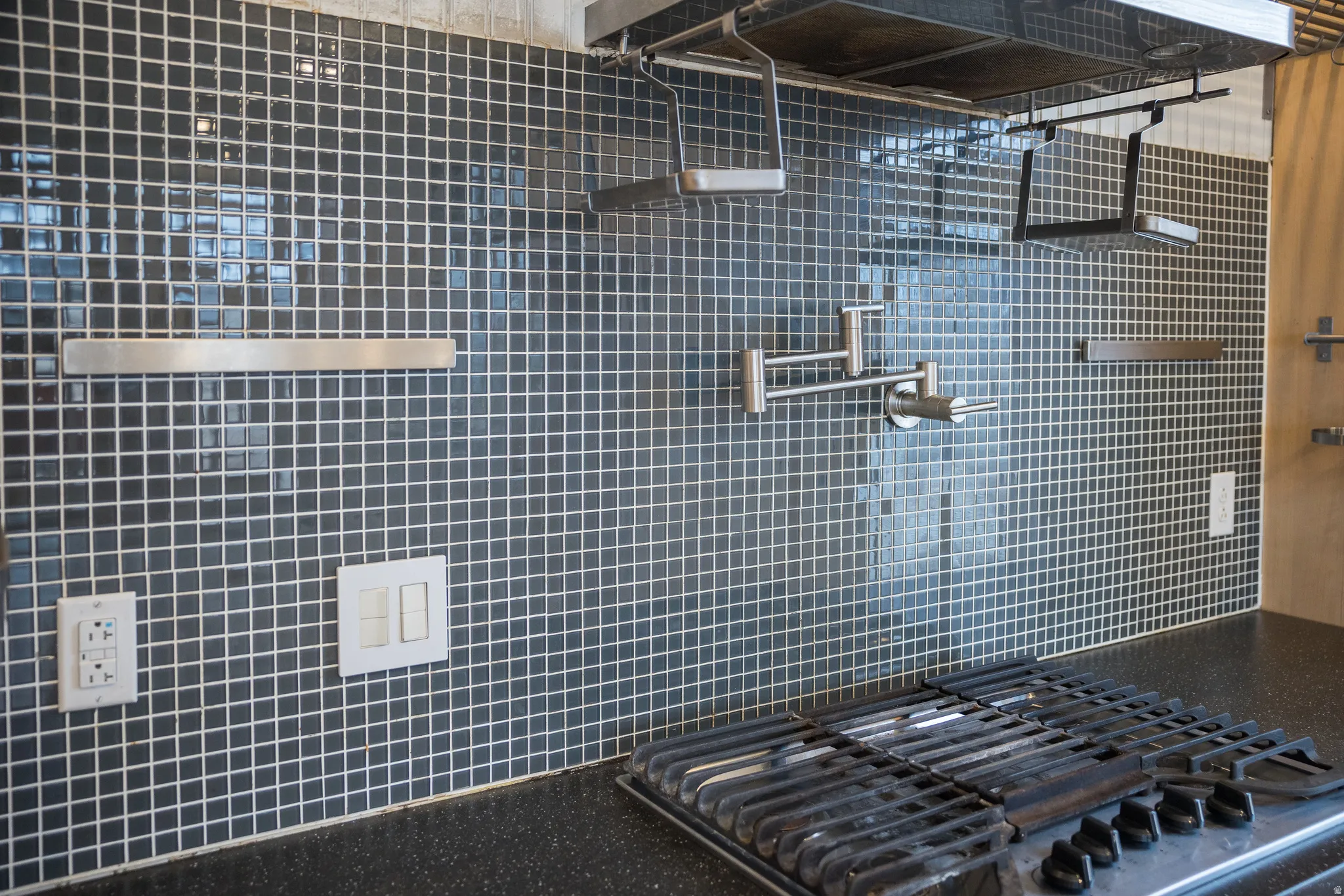 Kitchen view of pot filler, exhaust hood, and stainless steel gas cooktop