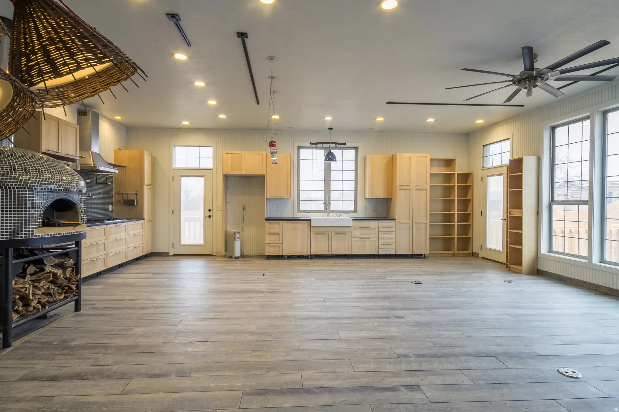 Kitchen with dark countertops, light wood finish cabinetry, hanging light fixtures, backsplash, and light wood finished floors