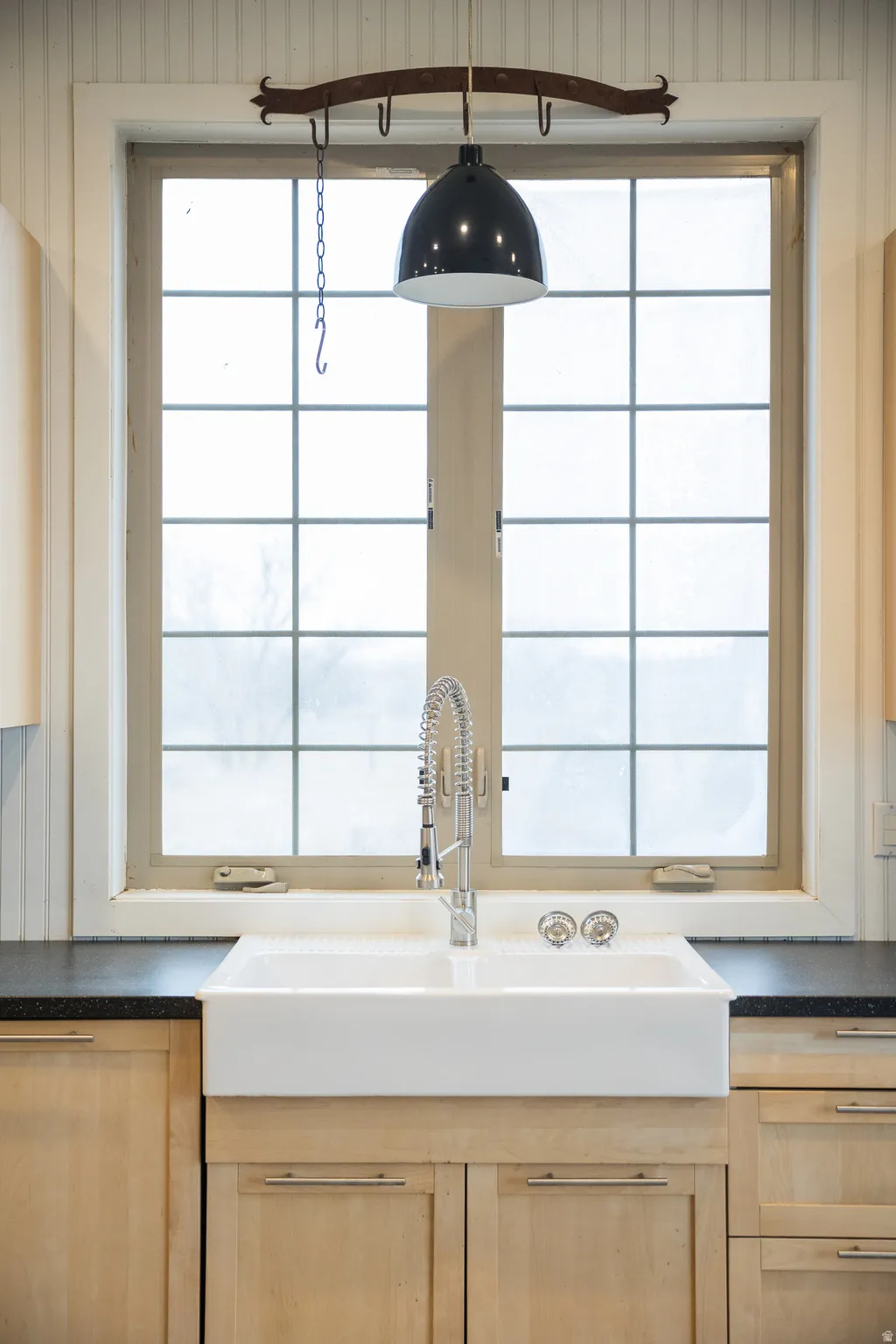 Kitchen view of dark countertops, light wood finish cabinetry, and hanging light fixtures