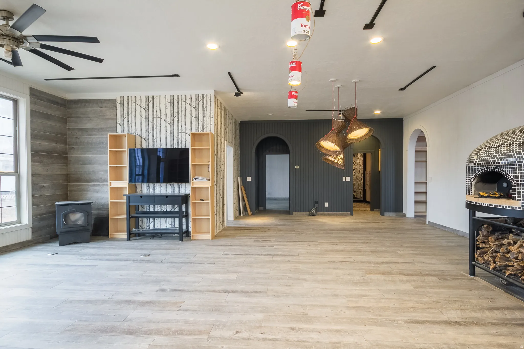 Living room with arched walkways, a wood stove, light wood-type flooring, ceiling fan, and recessed lighting