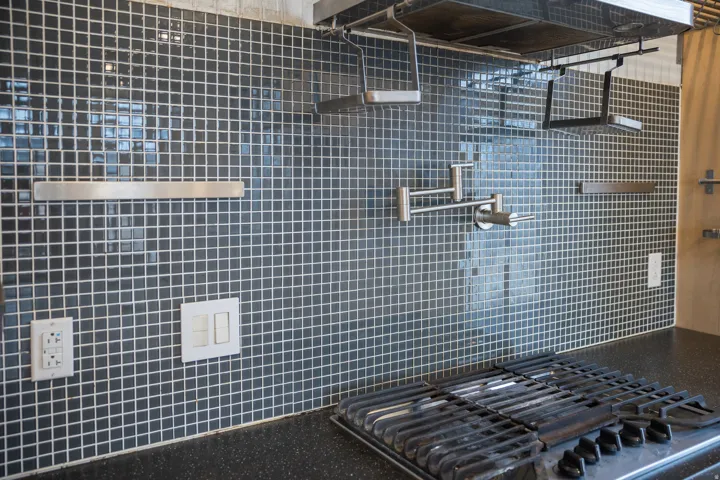 Kitchen view of pot filler, exhaust hood, and stainless steel gas cooktop