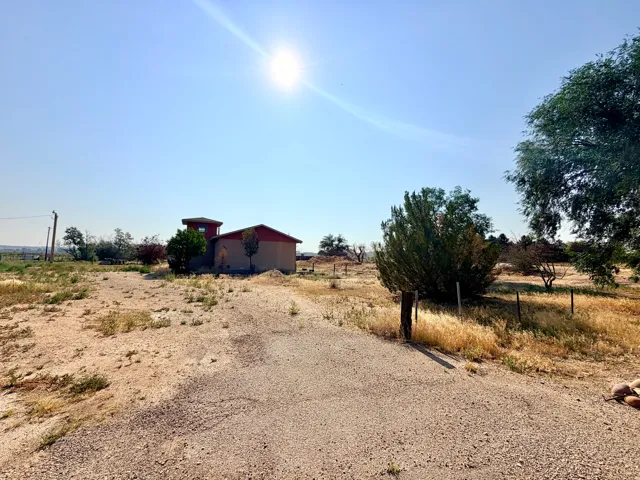 Gravel pathway leading to a stucco-finished building with a red roof, surrounded by natural landscaping and scattered mature trees