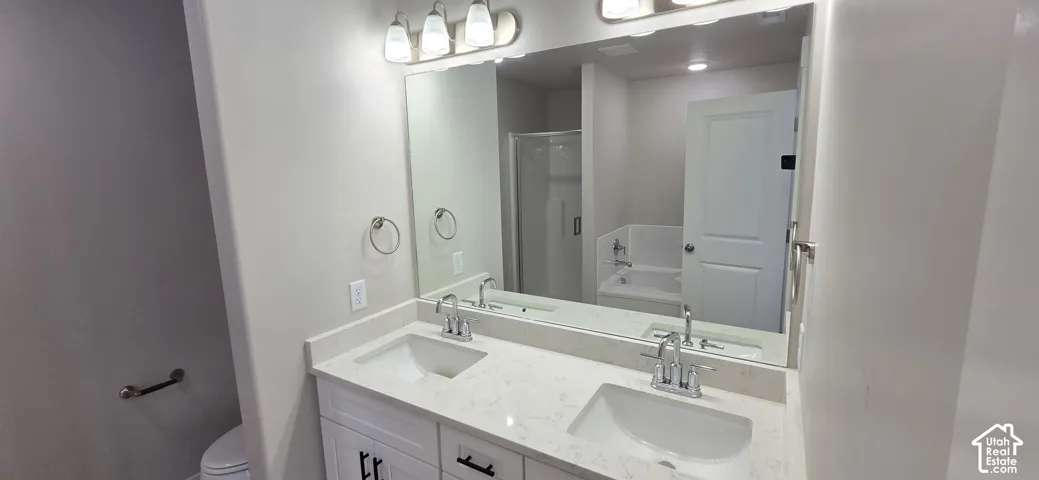 Dual vanity with integrated sinks, a large wall-mounted mirror, overhead light fixtures, and chrome hardware