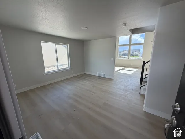 Wood-finish flooring throughout, bright interior with multiple windows, and a staircase with a black metal railing