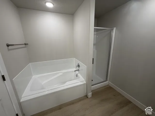 White soaking tub with deck-mounted fixtures, separate shower enclosure with clear glass door, wood-finish flooring, and recessed ceiling lighting