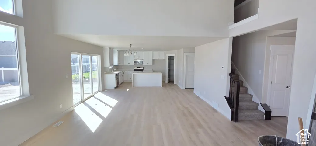 Vaulted ceilings, wood-finish flooring, white kitchen cabinetry, sliding glass doors, and a staircase with wood railing