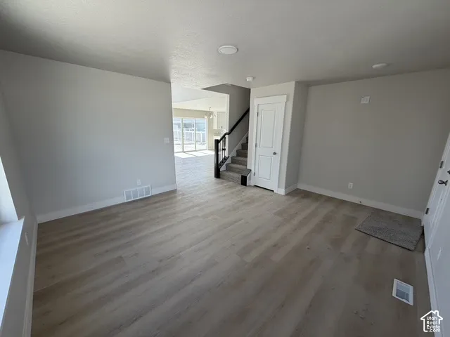 Wood-finish flooring, staircase with dark handrail, recessed lighting, and light neutral wall finishes