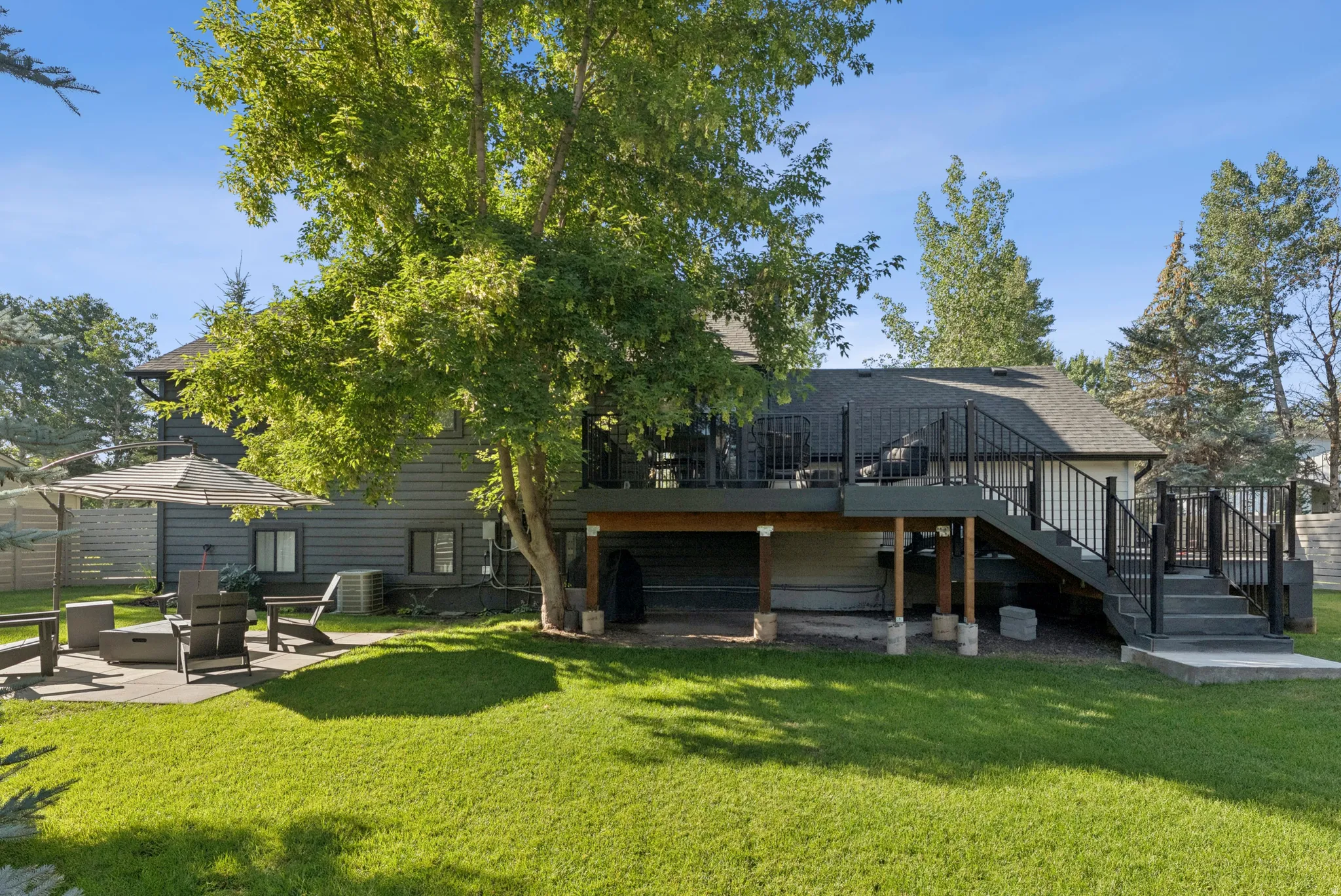 Back of property featuring a patio area, a yard, a deck, and roof with shingles