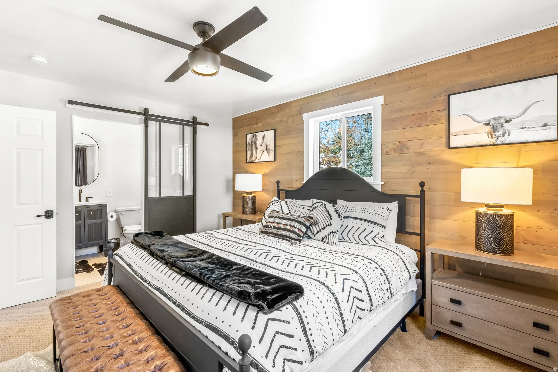 Bedroom featuring wood walls, light carpet, ensuite bathroom, ceiling fan, and a barn door