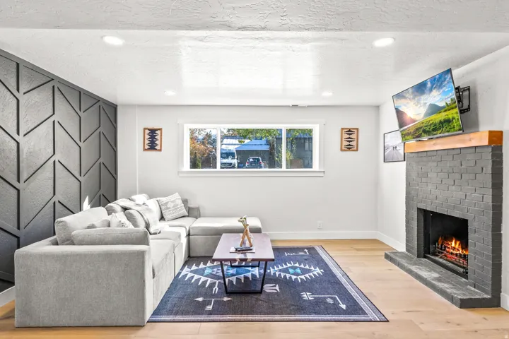 Living room with light wood-type flooring, a brick fireplace, an accent wall, recessed lighting, and a textured ceiling