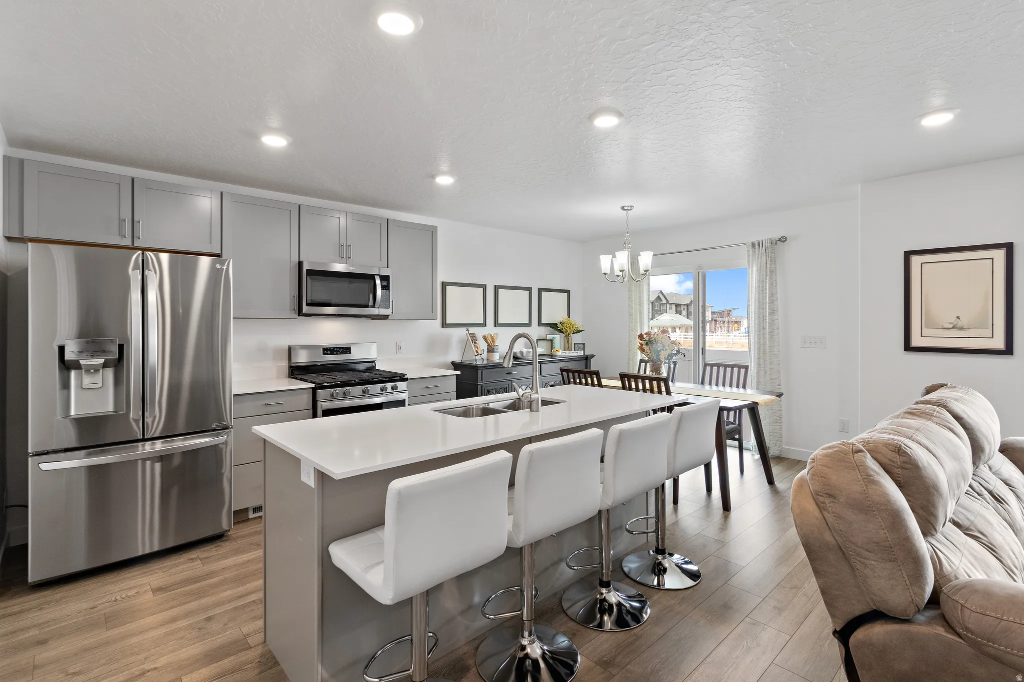 Kitchen with stainless steel appliances, gray cabinetry, open floor plan, an island with sink, and a textured ceiling