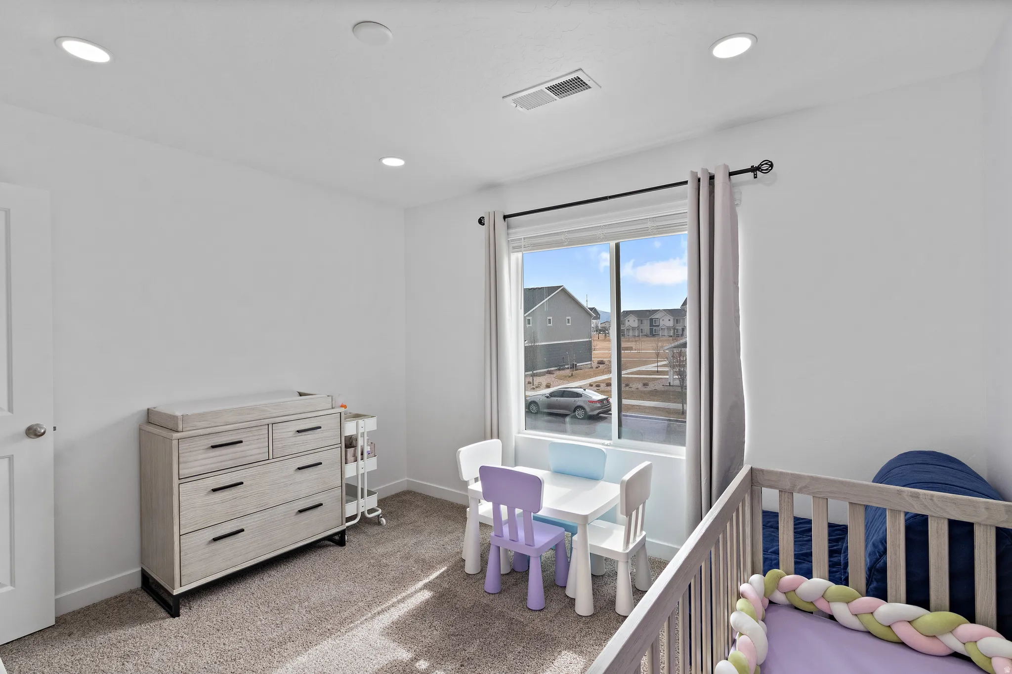 Carpeted bedroom with a crib and recessed lighting